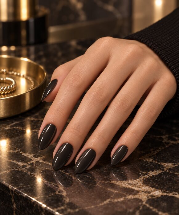 Glossy black almond nails resting on black and gold marble